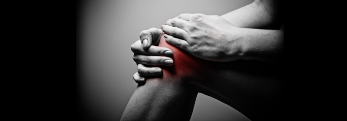Black and white image of hands clutching a knee with a red highlighted area indicating severe joint inflammation.