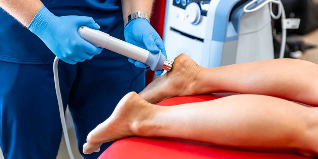 Healthcare provider using a handheld shockwave therapy device on a patient's heel to treat plantar fasciitis.
