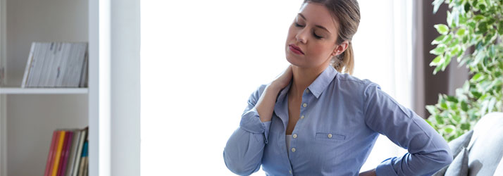 Woman in blue shirt massaging her neck and back in pain, illustrating helpful relief tips from a Medway chiropractor.