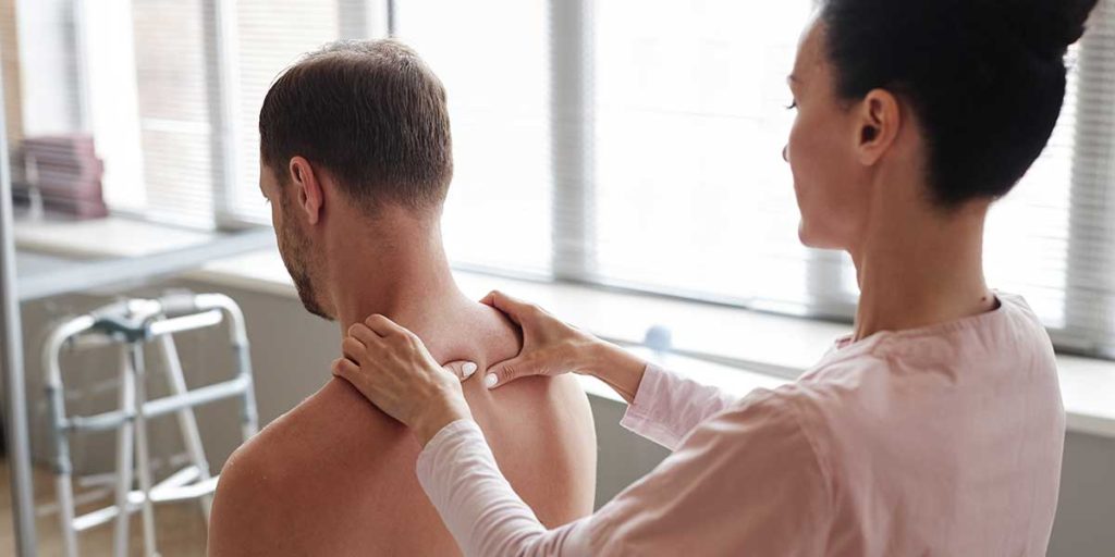 Female chiropractor examining and massaging the base of a man's neck and upper back during a clinical assessment.