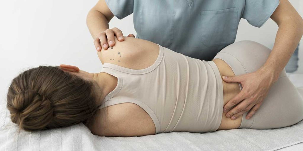 Therapist gently applying hands to the shoulder and lower back of a woman lying sideways on a massage table.