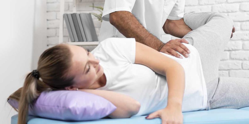 Chiropractor adjusting a woman lying on her side, manipulating her bent knee and lower back during a hip treatment session.