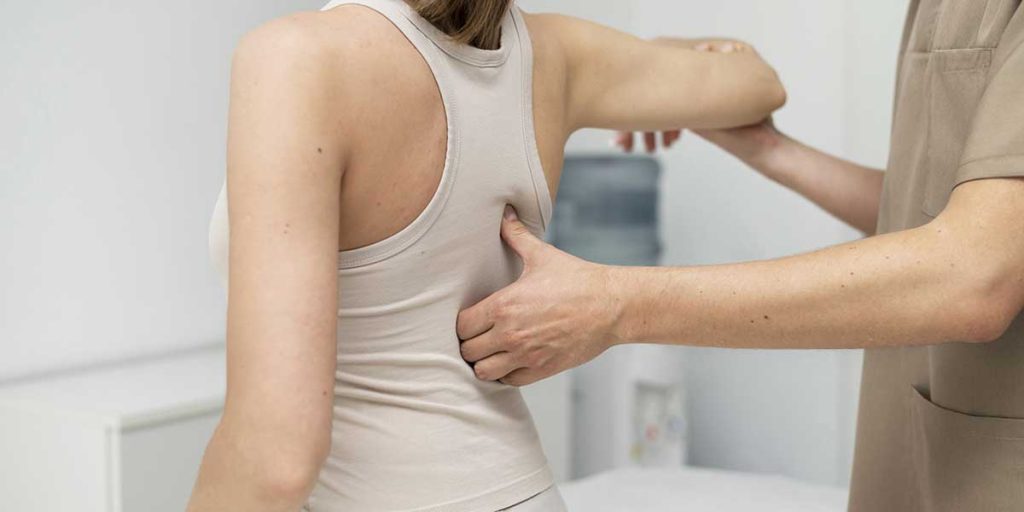 Physical therapist evaluating a woman's spine while gently lifting her arm during a non-surgical spinal decompression session.