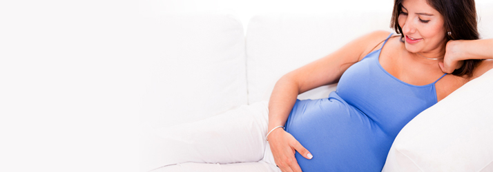 Pregnant woman in blue tank top resting comfortably on a sofa, seeking gentle pregnancy chiropractic help in Medway area.