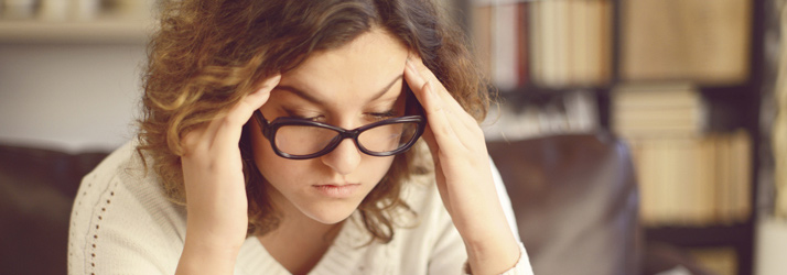 Woman with glasses holding her head in pain, illustrating chiropractic care solutions for relief from headaches in Medway area.