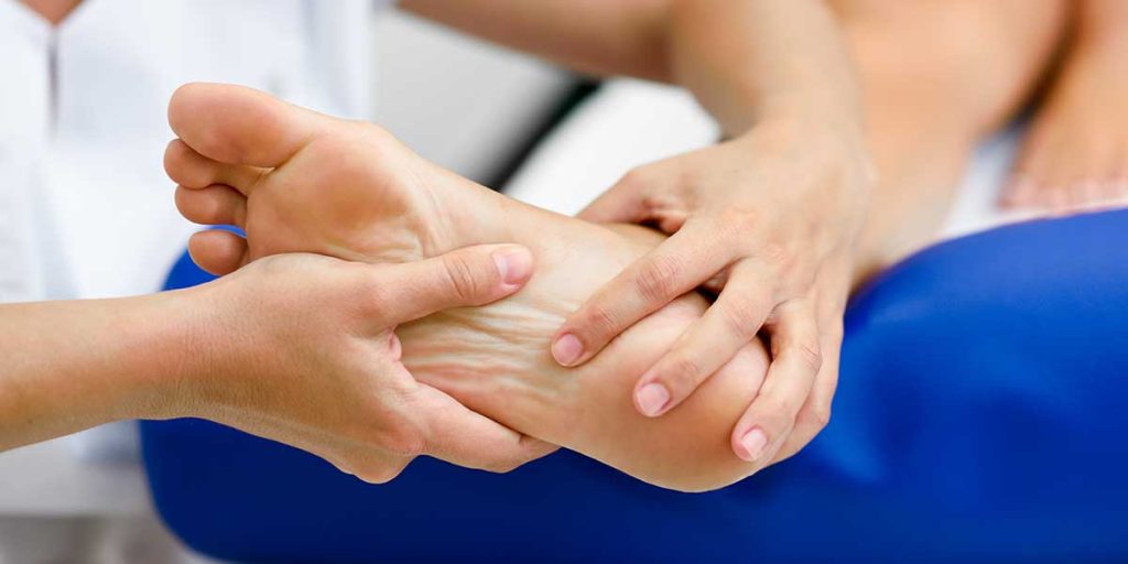 A physical therapist examines and massages a patient's foot sole to relieve pain caused by plantar fasciitis.