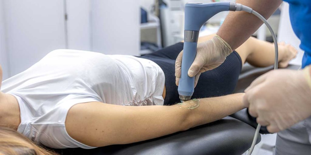 A clinician applies a shockwave therapy device to a patient's arm to relieve pain caused by tennis elbow.